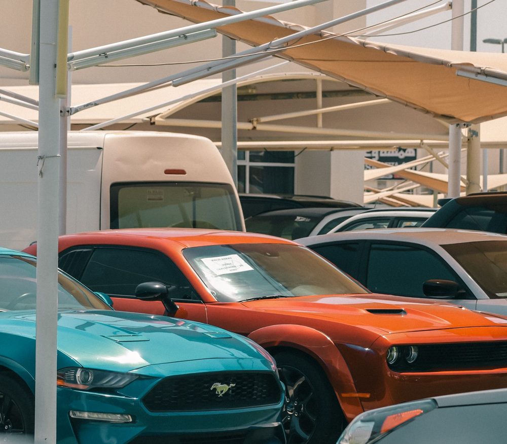 Late-model coupes and SUVs parked in rows under a dealer canopy