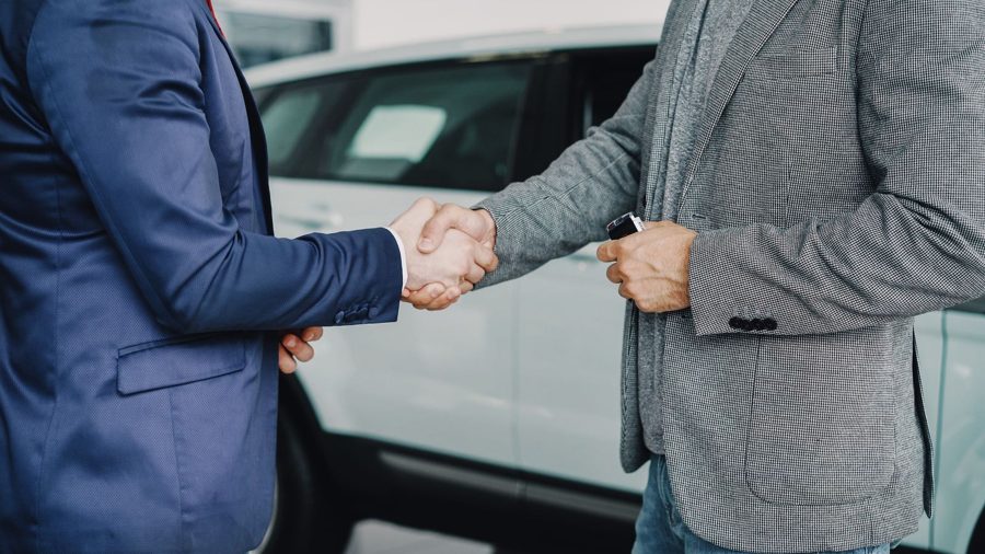 Two people shaking hands next to a car, keys in hand